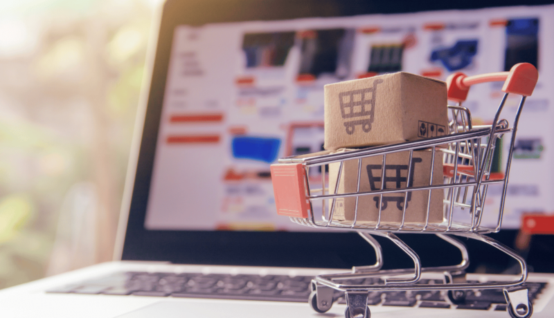 Laptop with online shopping and a small shopping cart with boxes on top